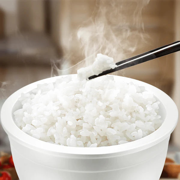 White bowl of steaming rice with chopsticks on a blurred background