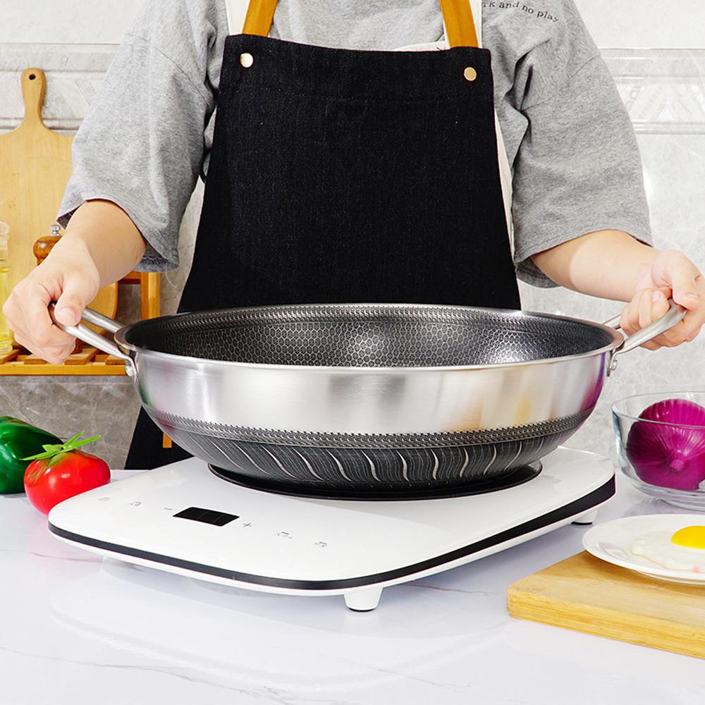 Person holding a large metal wok on a white surface with kitchen items around