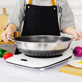 Person holding a large metal wok on a white surface with kitchen items around