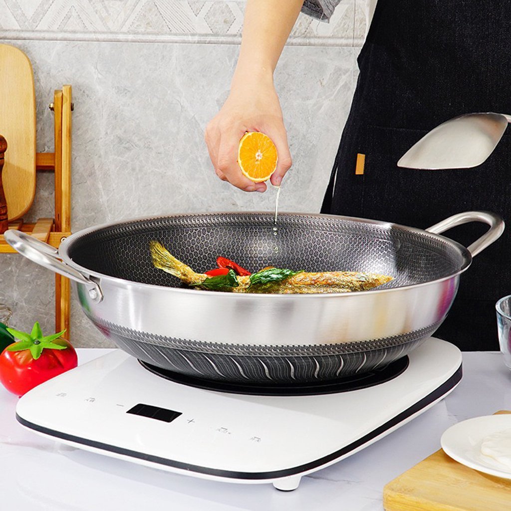 Person cooking fish in a wok on a portable stove with a kitchen setting in the background.