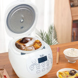 White rice cooker with food on a wooden table, surrounded by bowls and chopsticks.