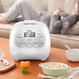 White Kylin rice cooker on a wooden table with a bowl of food and a person in the background.